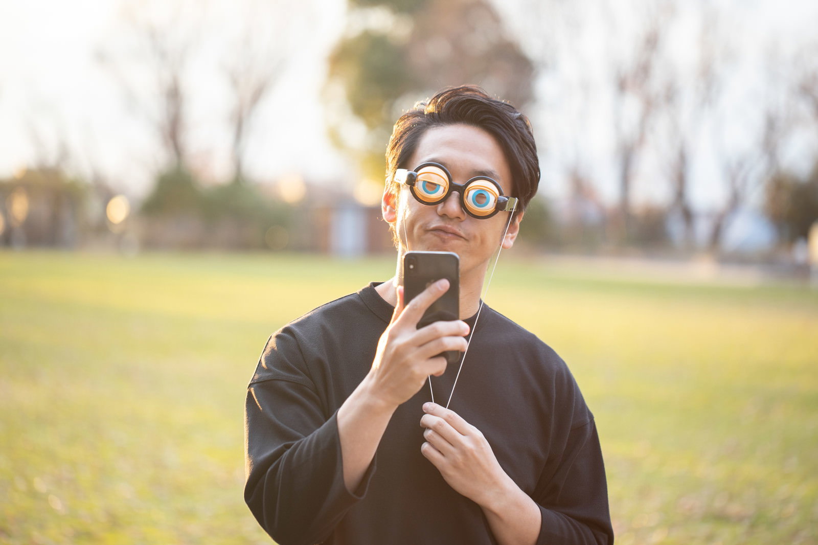 大きな目玉のアイテムを持ちスマホを見てニヤニヤする男性［モデル：大川竜弥］