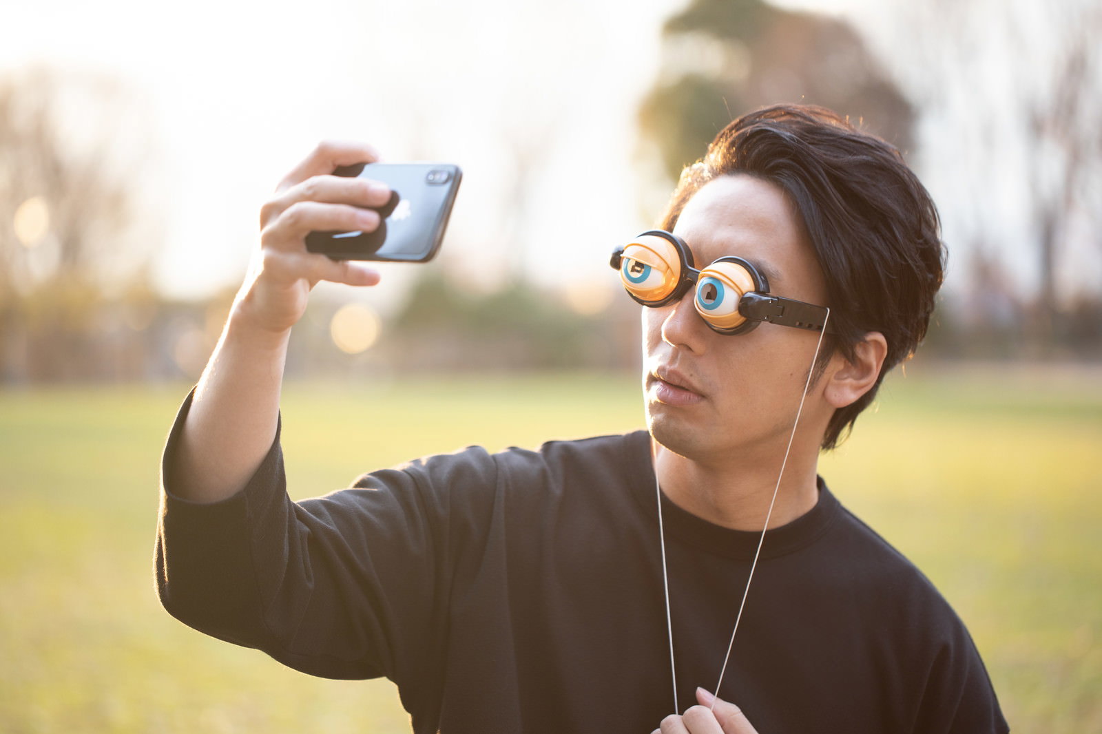 目玉の小道具を顔に当てながらセルフィーを撮る男性［モデル：大川竜弥］