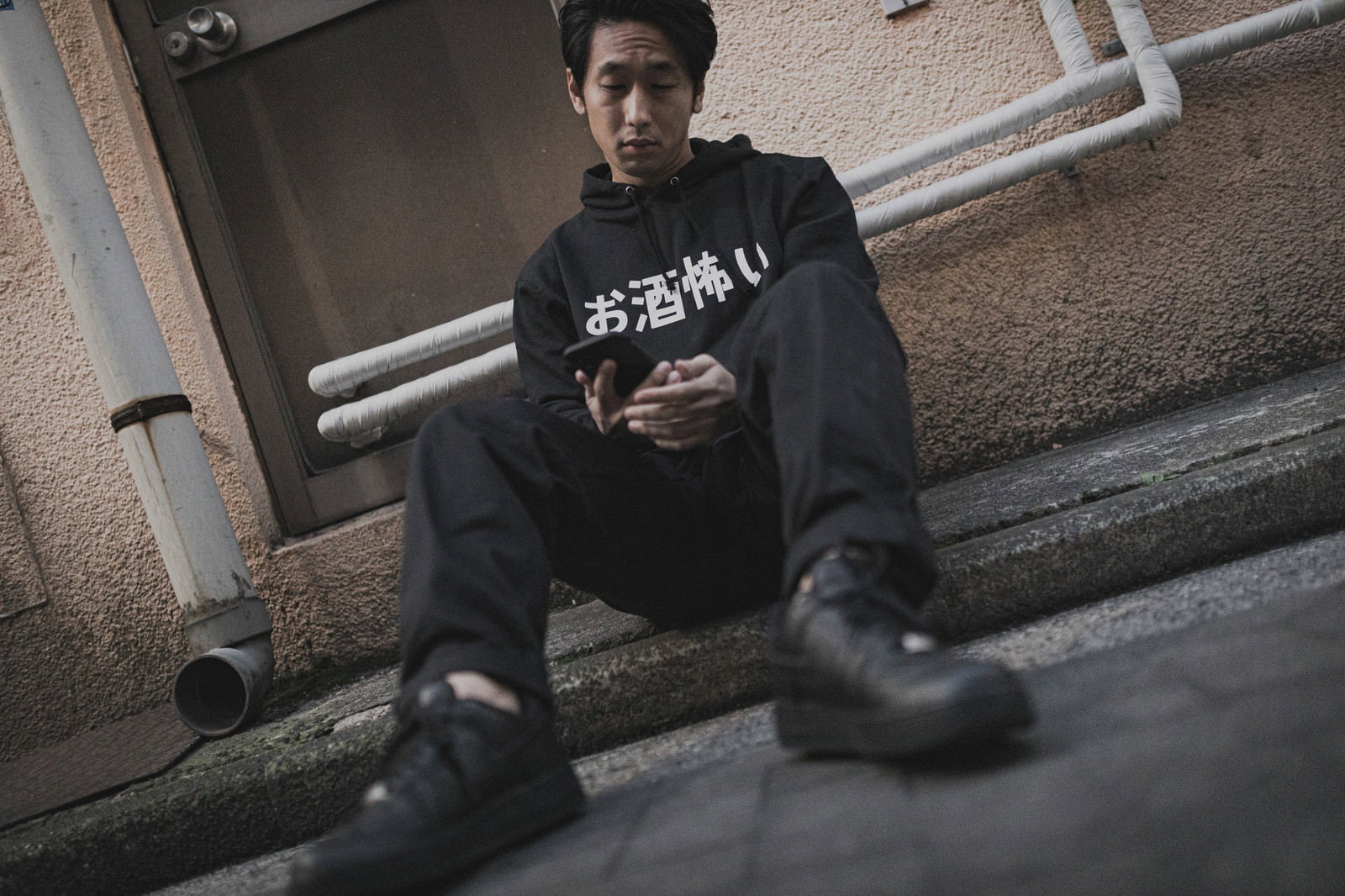 黒いスウェットを着た男性が路上の階段前に座り込んでいる［モデル：大川竜弥］