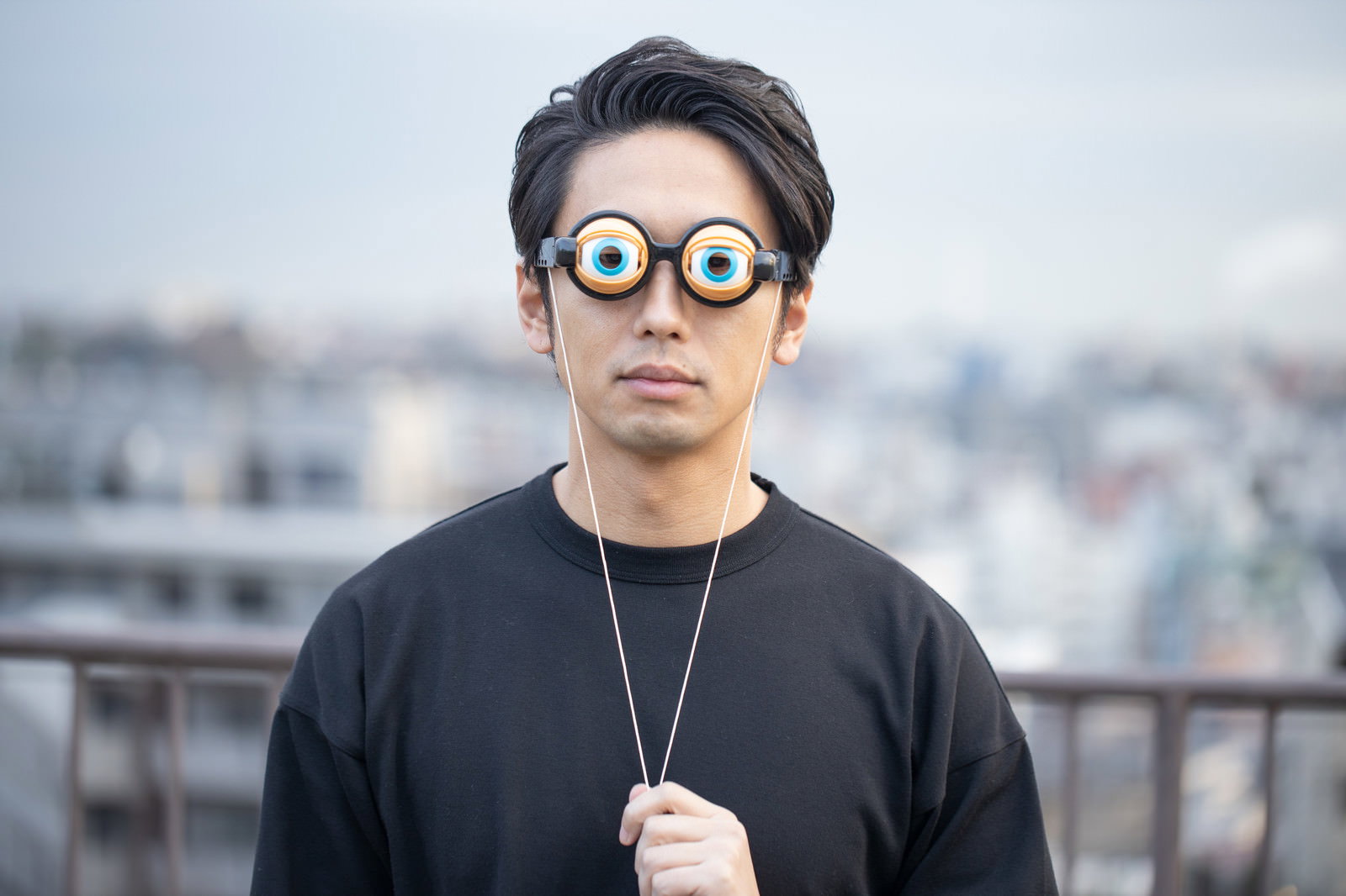 大きな目玉模様の眼鏡をかけて黒いシャツを着た男性［モデル：大川竜弥］
