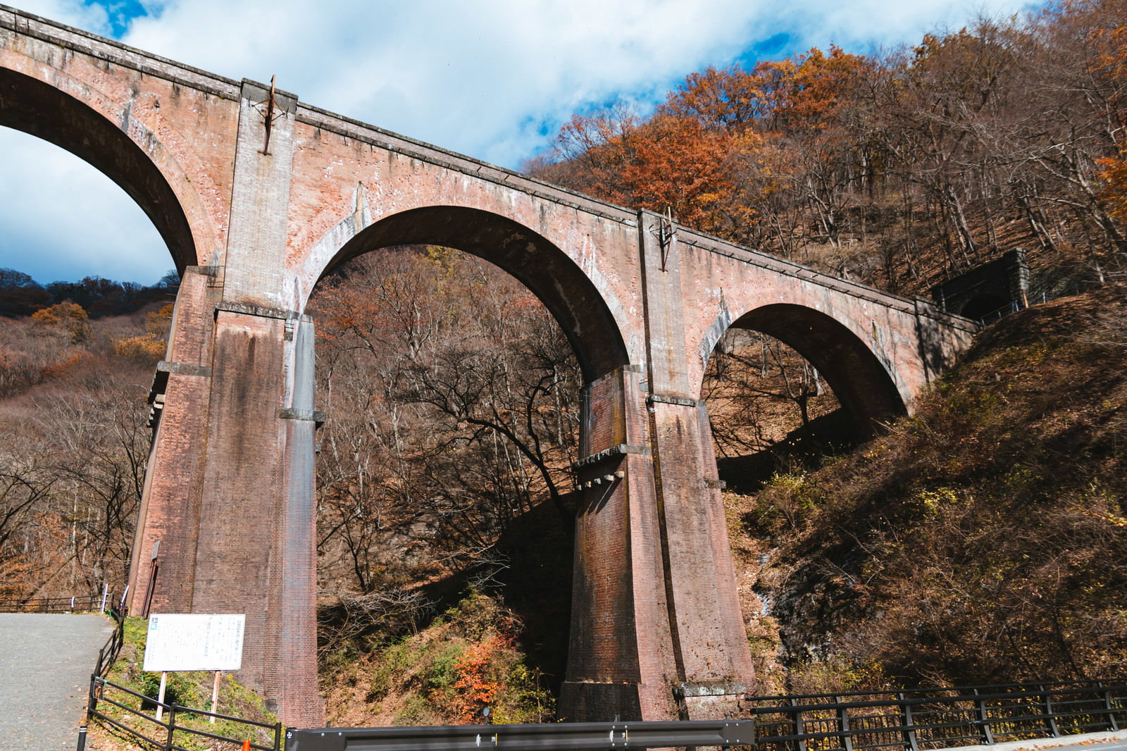 山間部の紅葉した景色に架かるアーチ型の石橋（めがね橋）
