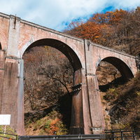 秋の群馬、紅葉に映えるアーチ型の石橋（めがね橋）の写真