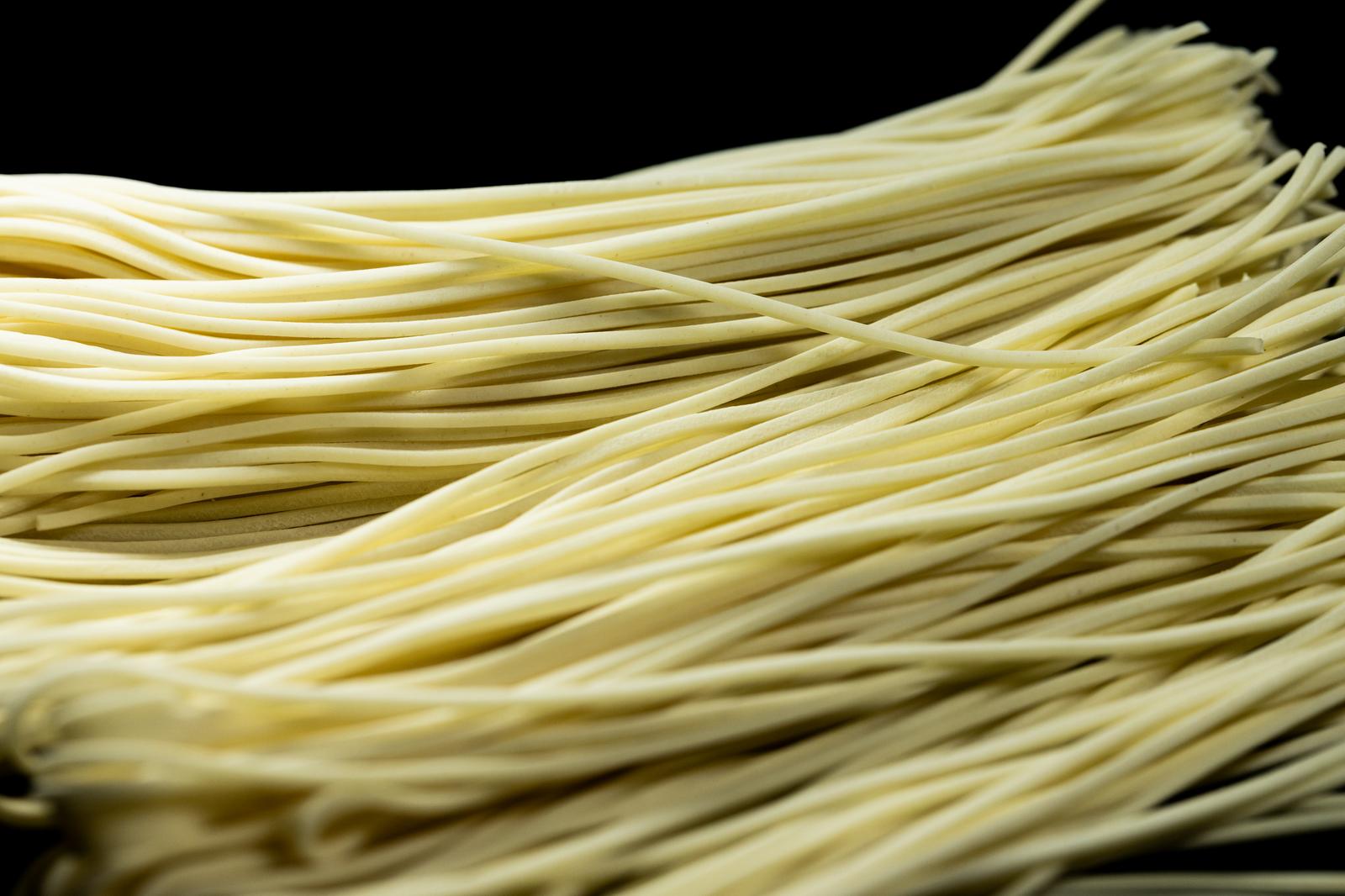 黒い背景の上に積み重ねられた淡黄色の乾麺の束