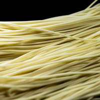 乾麺の黄色い束が重なり合う滑らかな質感と陰影の写真
