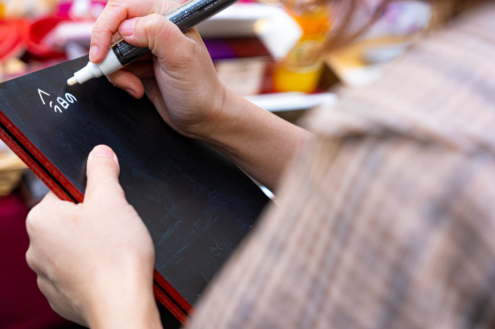 黒いメッセージボードに白いペンで文字を書き込む手元