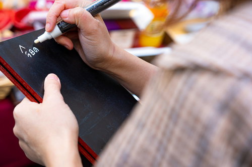 黒いメッセージボードに白いペンで書き込む手元