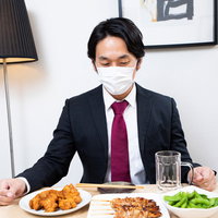 居酒屋のテーブルのおつまみを眺めるマスク着用の会社員の写真