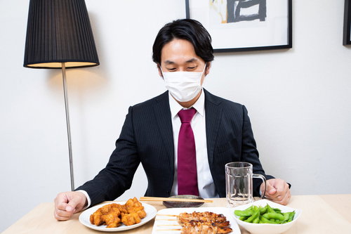 居酒屋のテーブルのおつまみを眺めるマスク着用の会社員