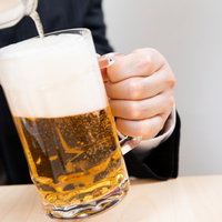 傾けたビールジョッキに注ぐ泡立つビール、黄金色の液体が流れ込むの写真