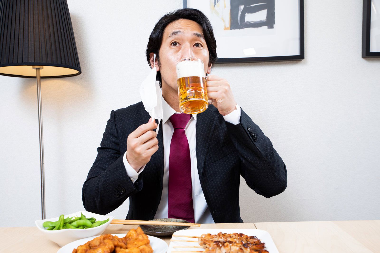 スーツ姿の会社員がマスクをずらして生ビールを飲んでいる様子［モデル：大川竜弥］