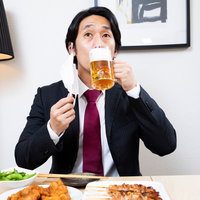 マスクをずらして生ビールを飲む会社員男性の写真