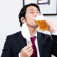 マスクを外してジョッキで生ビールをゴクゴク飲むサラリーマンの写真