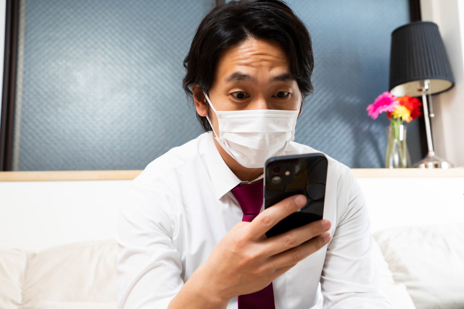 白いマスクを着けてスマートフォンを見つめる男性［モデル：大川竜弥］