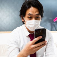 スマートフォンを凝視するマスク着用の会社員男性の写真