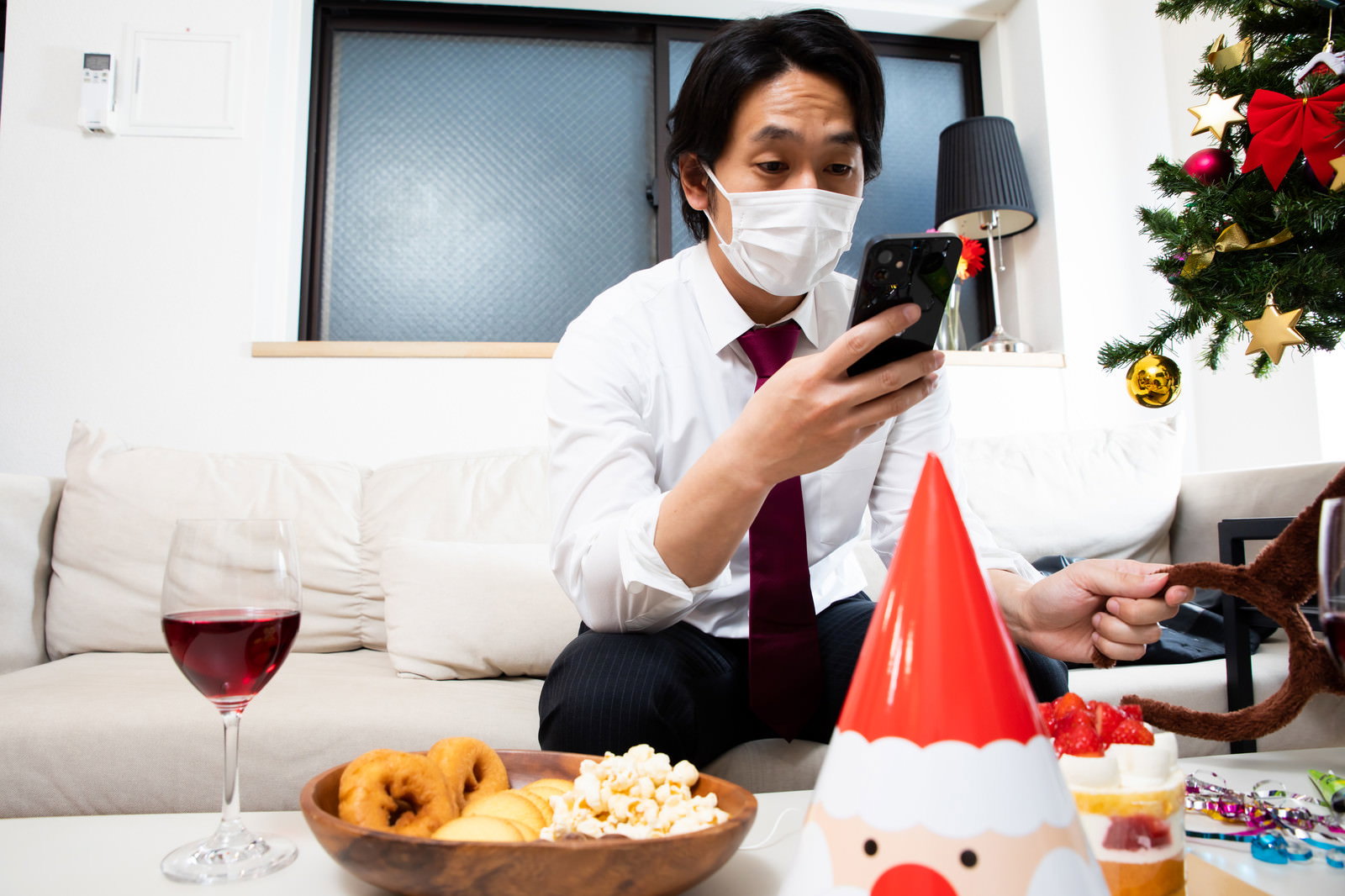 マスクをしてテーブルでスマートフォンを見ている男性［モデル：大川竜弥］