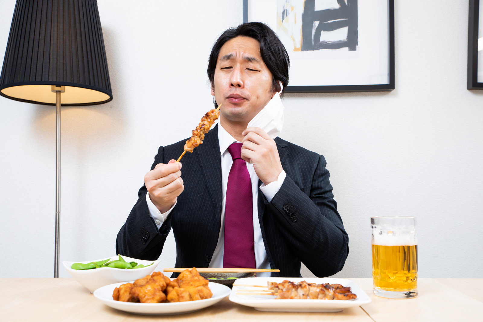 マスクを着用したサラリーマンが焼き鳥を食べている様子［モデル：大川竜弥］