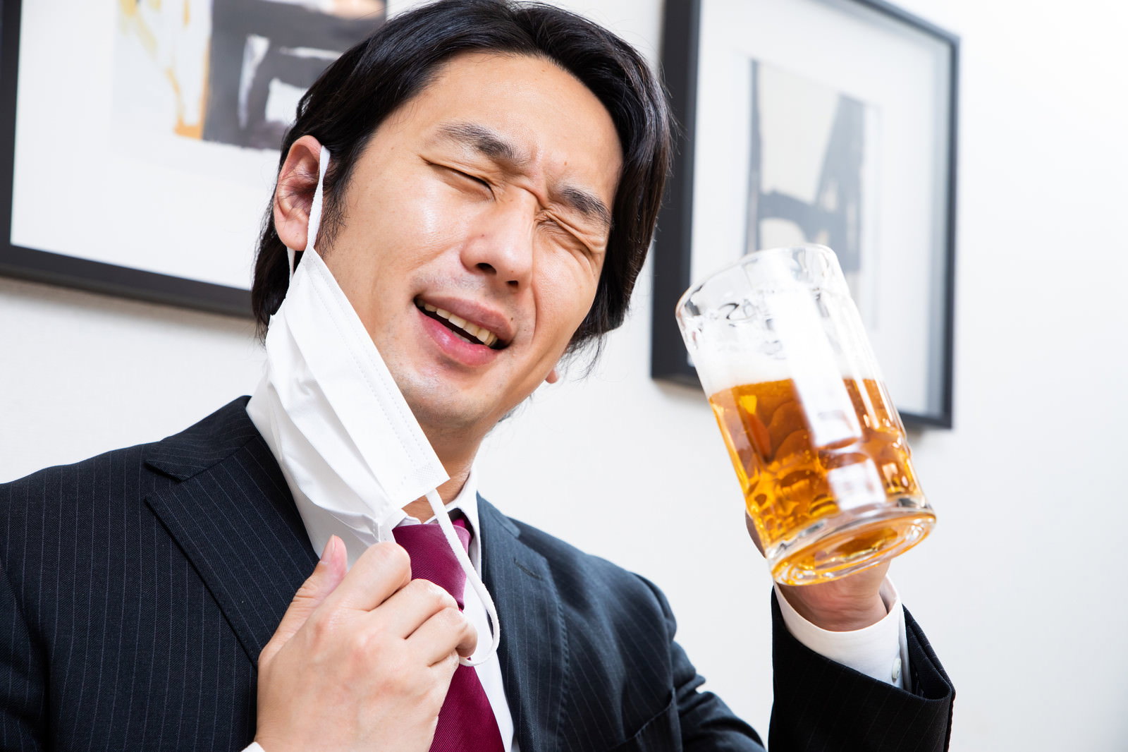 生ビールのジョッキを持って上機嫌な表情を見せるスーツ姿の会社員男性［モデル：大川竜弥］