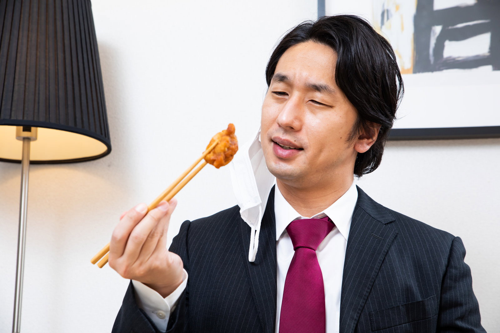 マスクを外して唐揚げを食べようとするスーツ姿の会社員男性［モデル：大川竜弥］