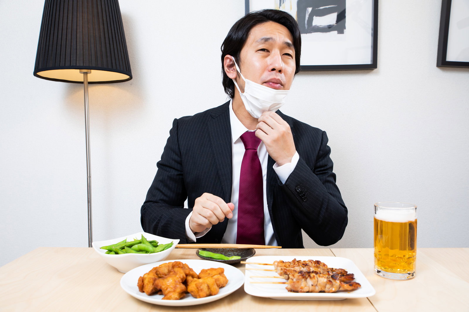 飲み会でマスクをずらしながら食事をするスーツ姿の会社員男性［モデル：大川竜弥］