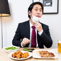 飲み会でマスクをずらして生ビールを飲む会社員の写真