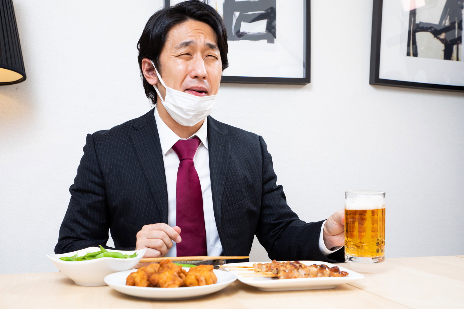 居酒屋でスーツ姿の男性が生ビールジョッキを手に笑顔でくつろぐ様子［モデル：大川竜弥］