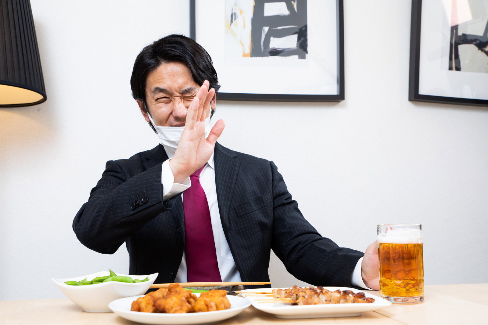 マスクを着用したスーツ姿の会社員が生ビールジョッキの前で手を上げて断る様子［モデル：大川竜弥］
