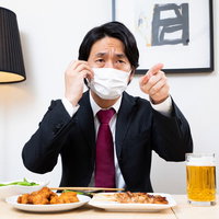 忘年会中にマスク姿で指を差す上司と生ビールの写真