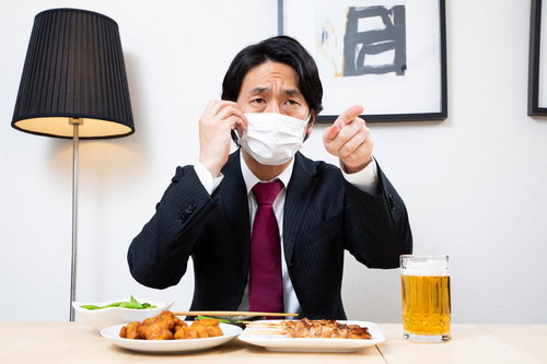 忘年会中にマスク姿で指を差す上司と生ビール