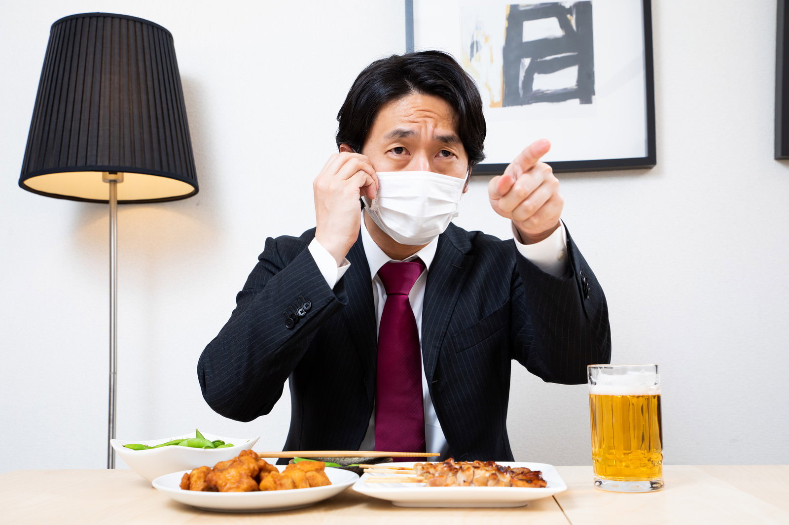 居酒屋でマスクをして指差しポーズをする会社員男性［モデル：大川竜弥］
