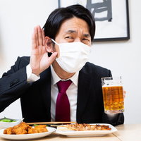 マスク越しの飲み会でよく聞こえない男性会社員の写真