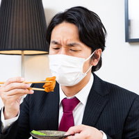 摘まんだ唐揚げをマスク越しに見つめる会社員男性の写真