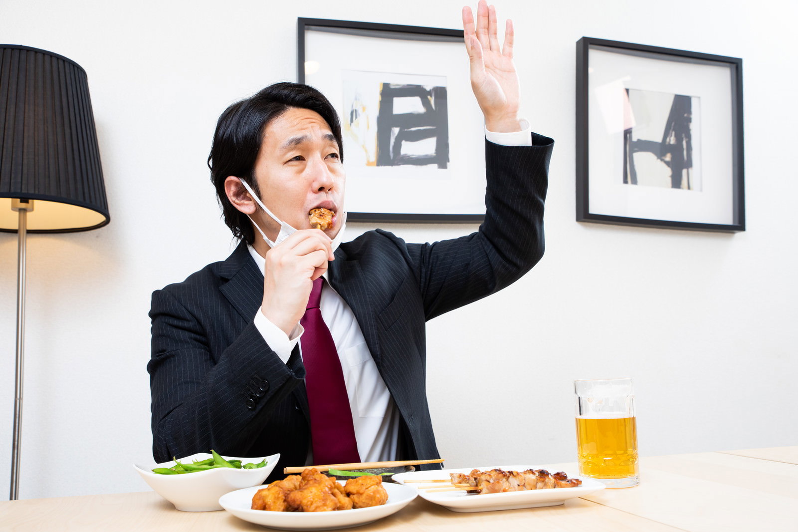 手を上げて追加注文をする会社員男性、テーブルに料理とビール［モデル：大川竜弥］