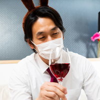 マスク姿でトナカイのカチューシャを身につけ赤ワインを飲む男性の写真