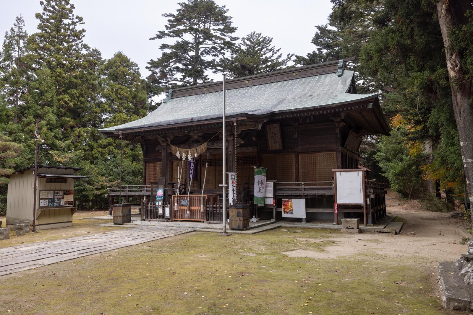 三春神社の本殿と参拝者向けのお堂が樹木に囲まれた境内に建つ写真