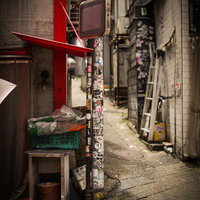 ステッカーだらけの電柱と古びた看板が目を引く裏路地の写真