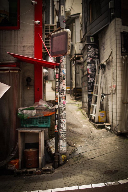 ステッカーだらけの電柱と古びた看板が目を引く裏路地
