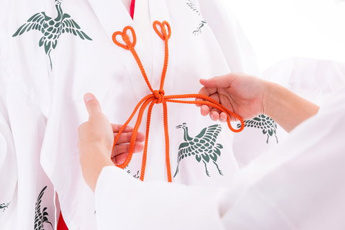 巫女の千早に赤い紐を結ぶ手元の作業風景