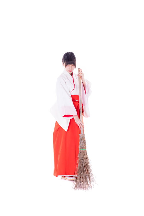 神社で竹箒を使い掃き掃除をする巫女