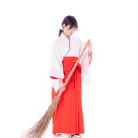 竹箒を持って掃除をはじめる巫女装束の女性の写真