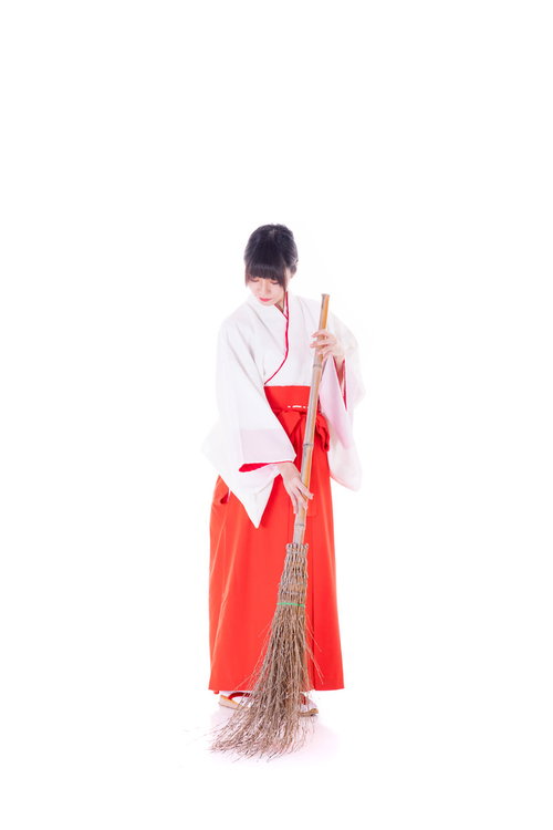 赤い袴姿の巫女さんが竹箒で掃除する様子 神社の参道