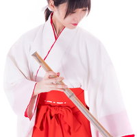 巫女装束を身に着けて竹箒で掃除する女性の神社清掃風景の写真