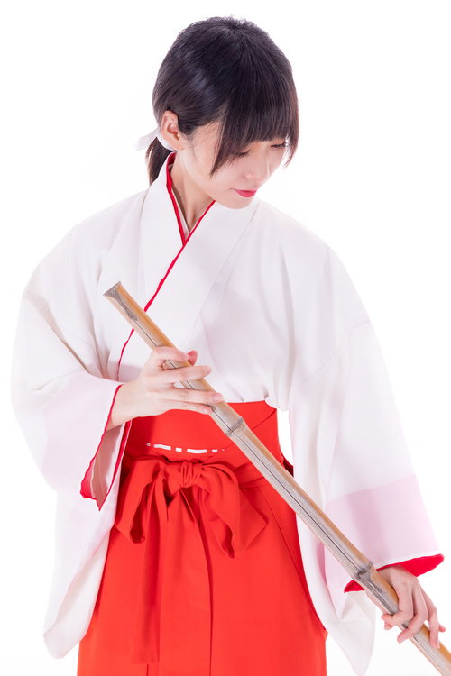 巫女装束を身に着けて竹箒で掃除する女性の神社清掃風景