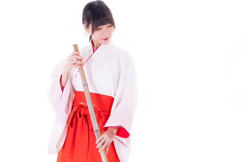 白と赤の巫女装束で竹箒の掃き掃除をする巫女さん