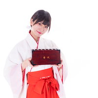 初詣で笑顔を見せる巫女が両手で賽銭箱を持ってきたの写真