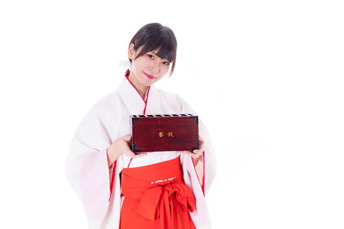 初詣で笑顔を見せる巫女が両手で賽銭箱を持ってきた