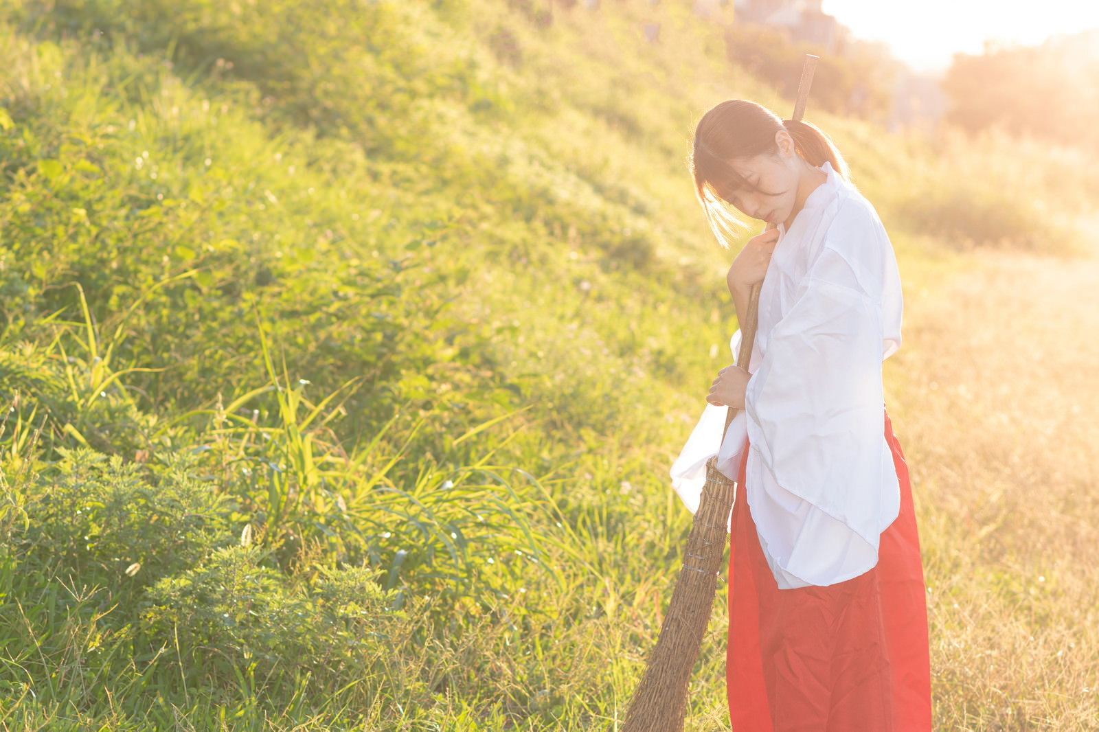Shrine maiden in red hakama sweeping with a bamboo broom at dusk