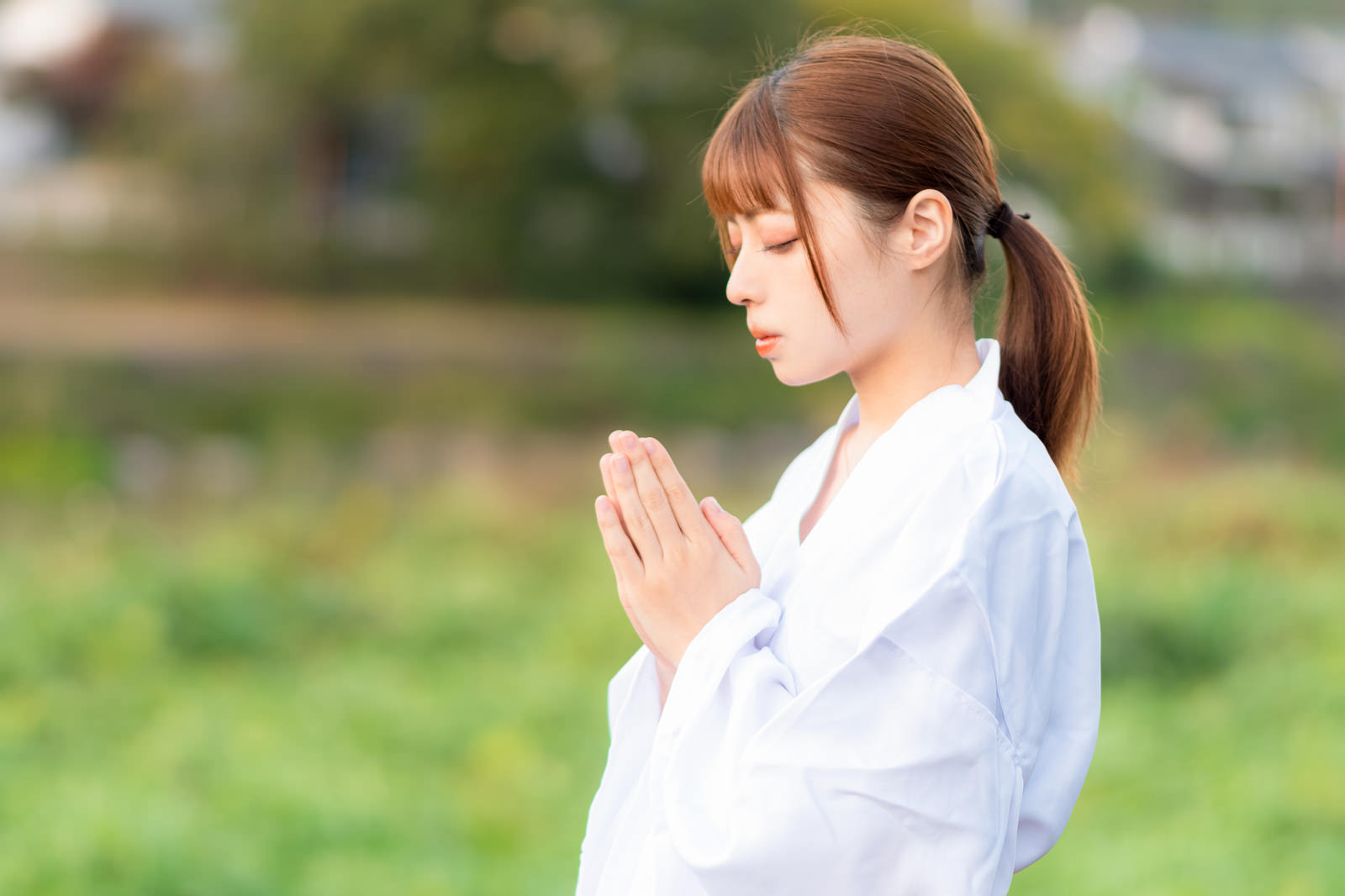 白い巫女装束を着た女性が目を閉じて手を合わせお祈りしている［モデル：高尾実生］