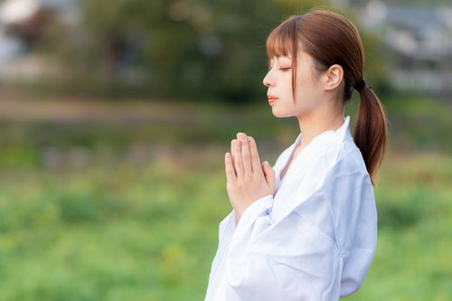 白い巫女装束で両手を合わせて目を閉じてお願いする女性