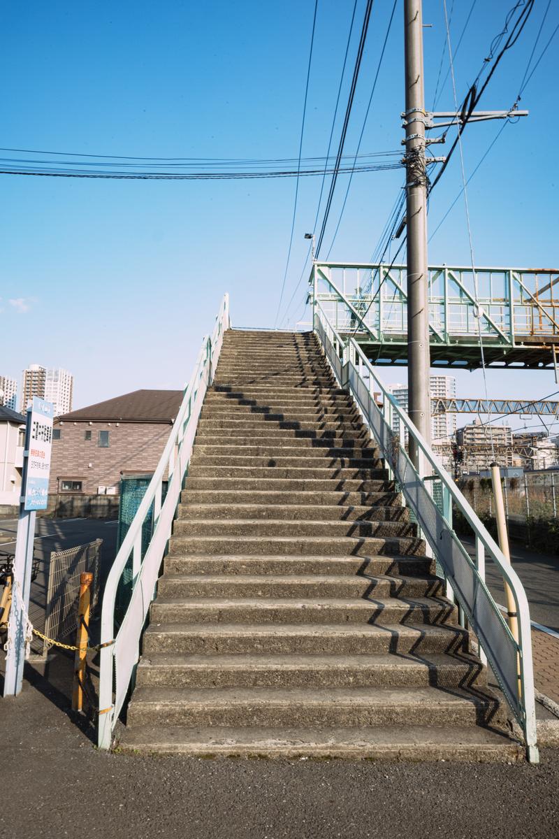 三鷹の跨線橋の階段。両側に手すり、上空に電力線と支柱が見える。