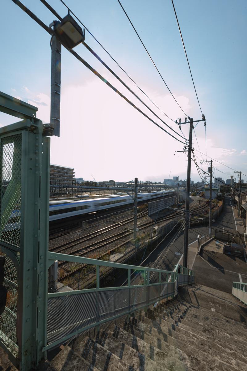 緑色の手すりと柵から見える複数の線路とJR電車、電柱がある風景